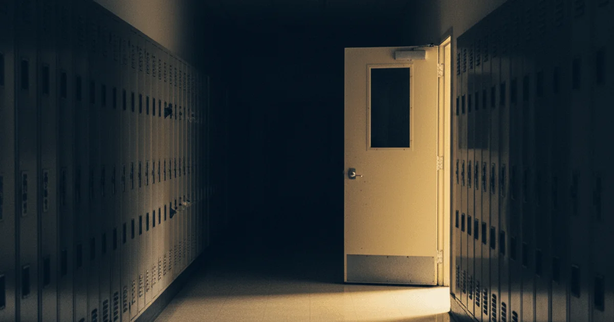 Empty school hallway at blue hour with amber light from classroom windows casting long shadows